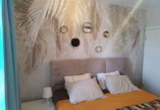 Элегантная спальня с морским пейзажем и декоративным панно, современный дизайн интерьера, уютная кровать с белыми подушками, ночной светильник, впечатляющие элементы декора и стильное оформление для комфортного отдыха.