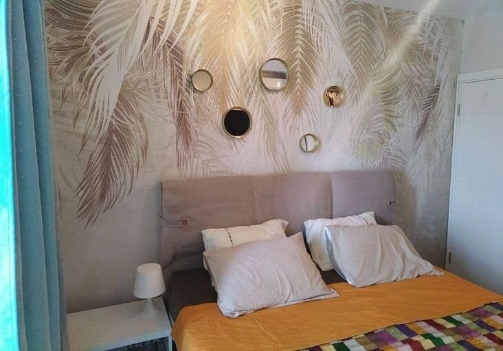 Элегантная спальня с морским пейзажем и декоративным панно, современный дизайн интерьера, уютная кровать с белыми подушками, ночной светильник, впечатляющие элементы декора и стильное оформление для комфортного отдыха.