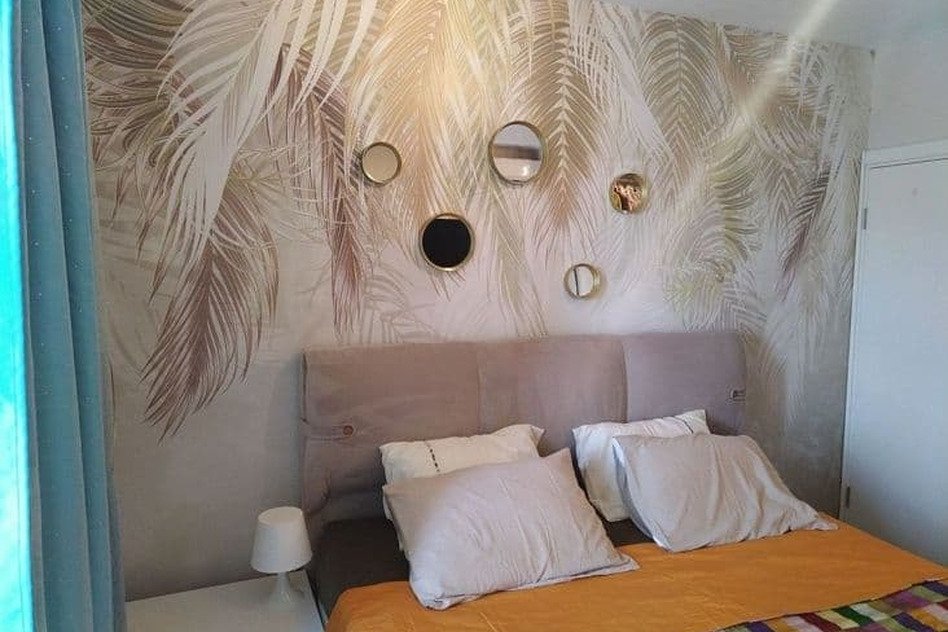 Элегантная спальня с морским пейзажем и декоративным панно, современный дизайн интерьера, уютная кровать с белыми подушками, ночной светильник, впечатляющие элементы декора и стильное оформление для комфортного отдыха.