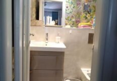 Маленькая современная ванная комната с зеркалом, цветами и предметами гигиены.