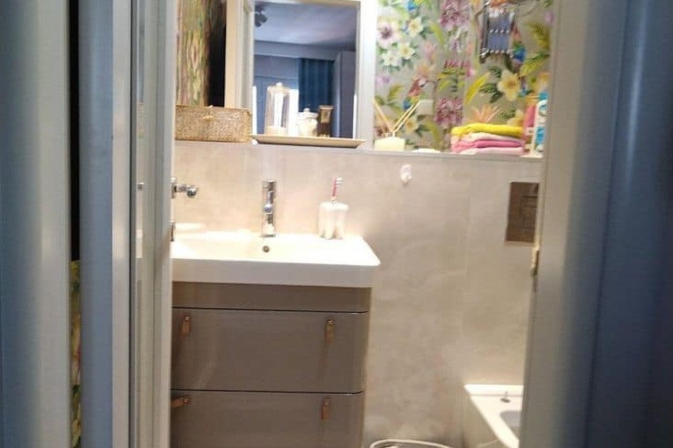 Маленькая современная ванная комната с зеркалом, цветами и предметами гигиены.