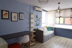 Красивая уютная комната с мягким диваном, яркими подушками и светлой отделкой, окна с жалюзи, стильное освещение и декоративные элементы для комфортного проживания.