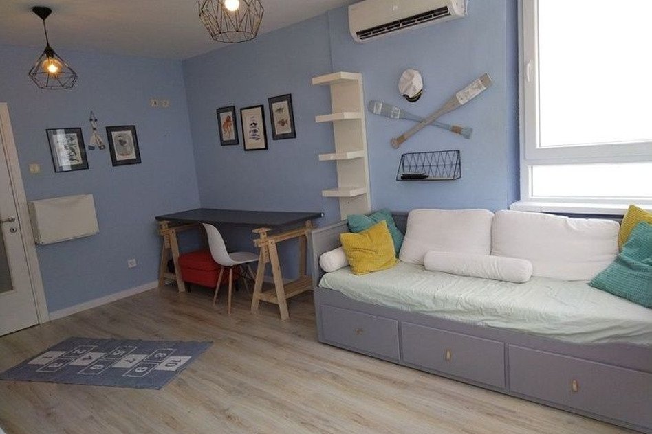 оригинальный интерьер гостиной с уютной мебелью и морской тематикой, светлая палитра и удобный диван с яркими подушками, стильные настенные украшения, большие окна для естественного освещения.