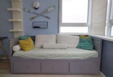 Комфортабельный диван-кровать в современной гостиной с яркими подушками и спортивной декорацией, оптимальное решение для уютного отдыха.