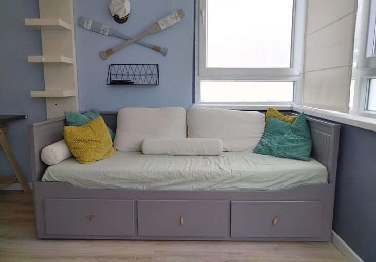 Комфортабельный диван-кровать в современной гостиной с яркими подушками и спортивной декорацией, оптимальное решение для уютного отдыха.