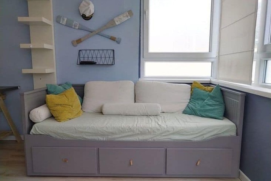 Комфортабельный диван-кровать в современной гостиной с яркими подушками и спортивной декорацией, оптимальное решение для уютного отдыха.