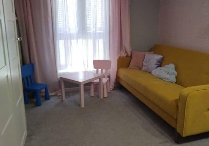 уютная гостиная комната с яркой желтой мягкой мебелью и детскими игрушками, светлый дизайн интерьера, большие окна с легкими шторами, приятная атмосфера для отдыха и развлечений в квартире Eurodomestate.com.