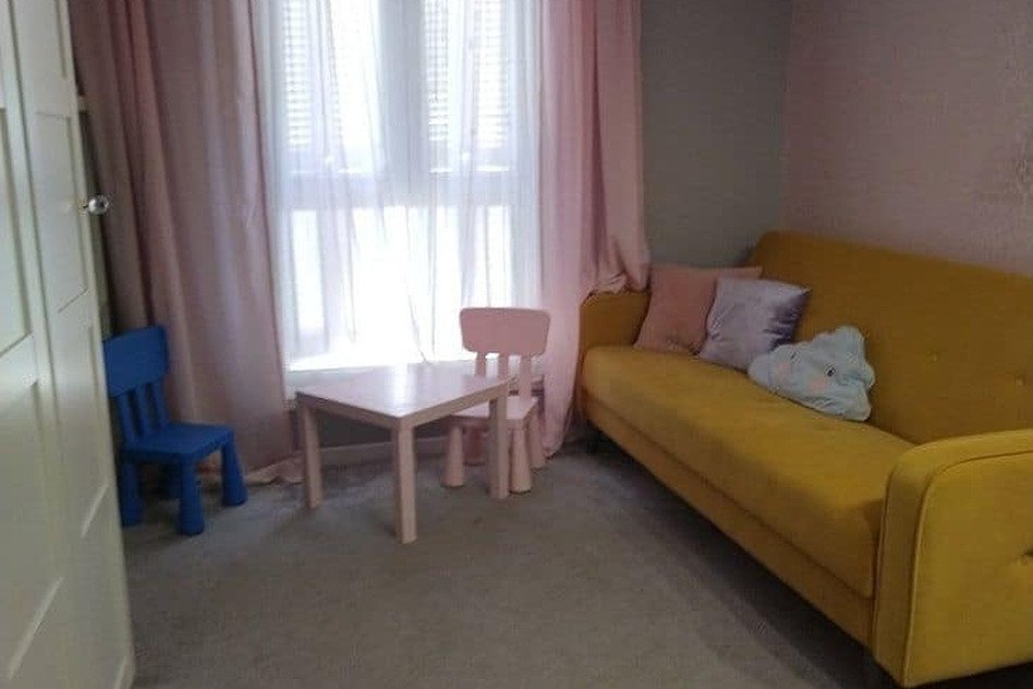 уютная гостиная комната с яркой желтой мягкой мебелью и детскими игрушками, светлый дизайн интерьера, большие окна с легкими шторами, приятная атмосфера для отдыха и развлечений в квартире Eurodomestate.com.