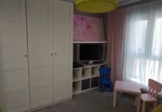 Детская комната с телевизором, шкафом и детской мебелью, уютное пространство для ребенка в современном стильном интерьере.