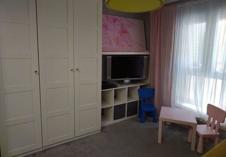 Детская комната с телевизором, шкафом и детской мебелью, уютное пространство для ребенка в современном стильном интерьере.